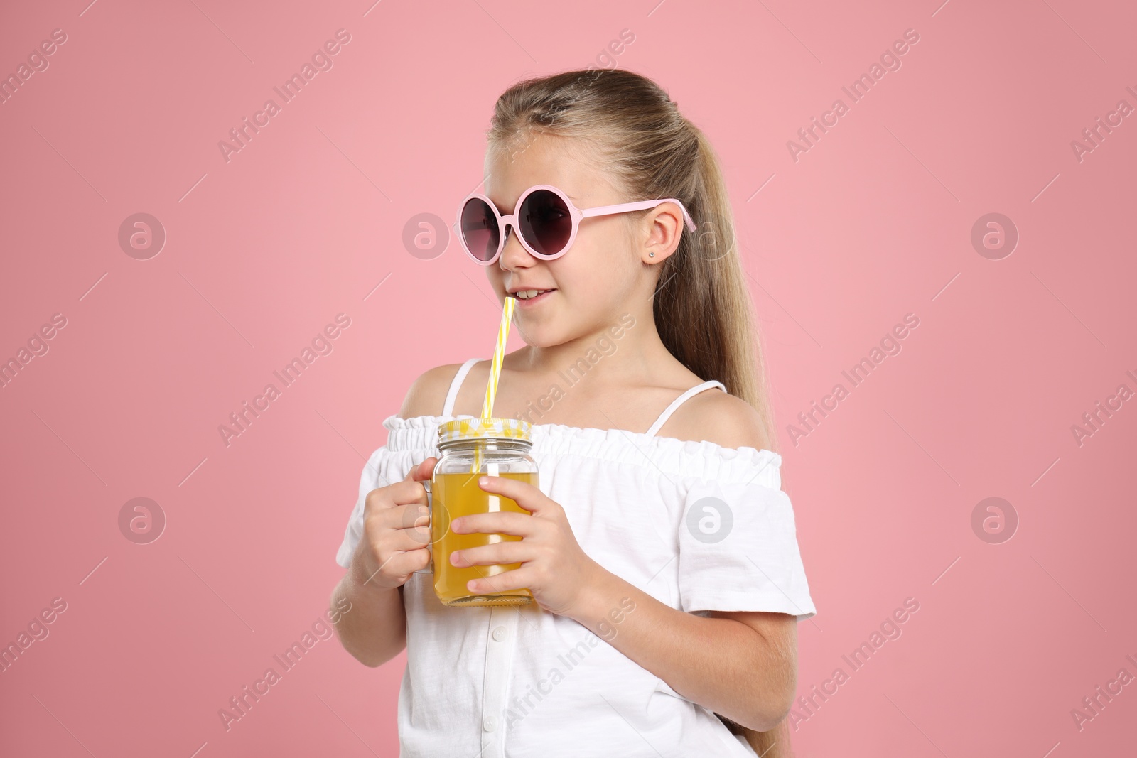 Photo of Little girl drinking juice through straw on pink background