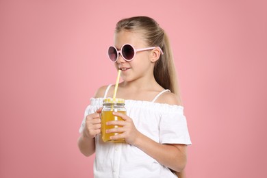 Photo of Little girl drinking juice through straw on pink background