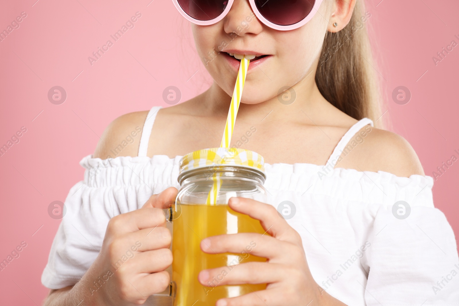 Photo of Little girl drinking juice through straw on pink background, closeup