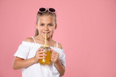 Photo of Little girl drinking juice through straw on pink background, space for text