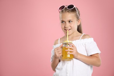 Photo of Little girl drinking juice through straw on pink background, space for text