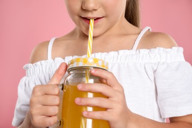 Photo of Little girl drinking juice through straw on pink background, closeup