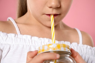 Photo of Little girl drinking refreshing drink through straw on pink background, closeup