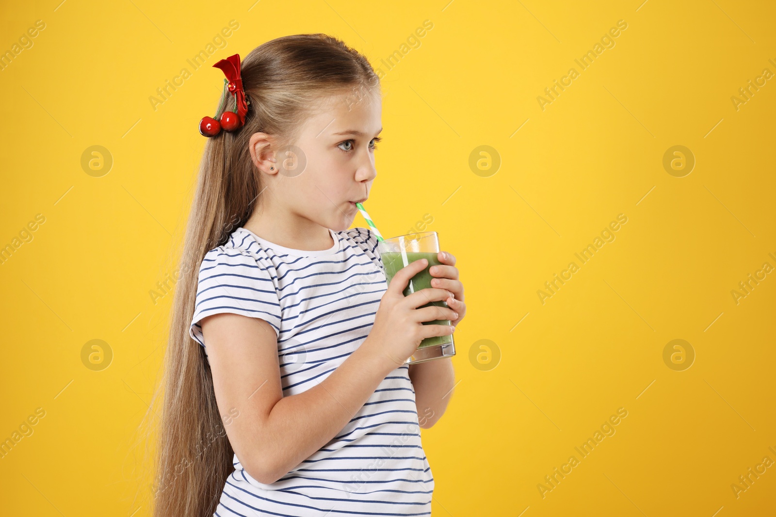 Photo of Little girl drinking juice through straw on orange background, space for text