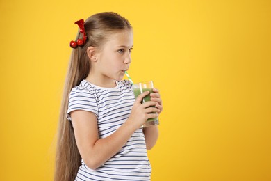 Photo of Little girl drinking juice through straw on orange background, space for text