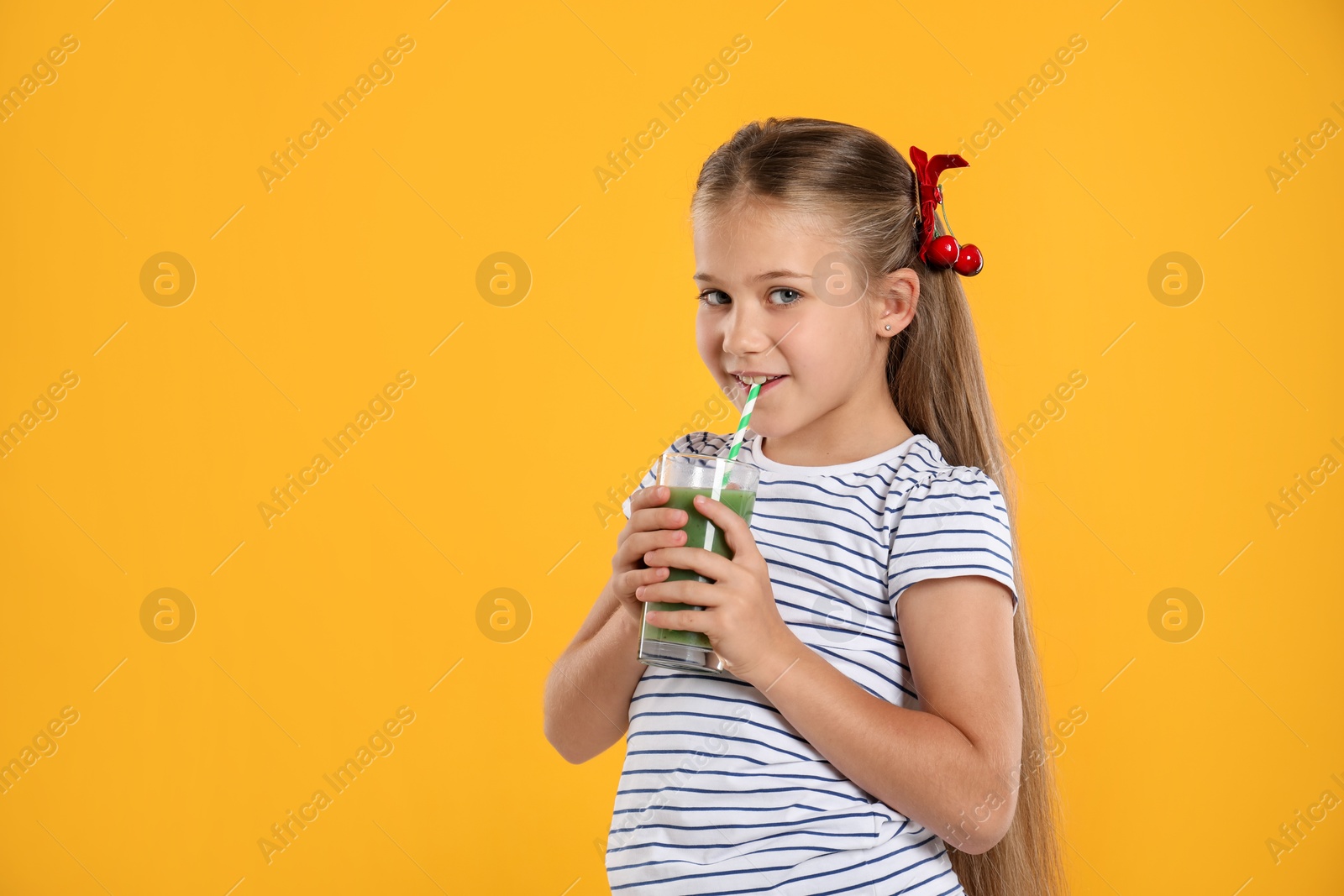 Photo of Little girl drinking juice through straw on orange background, space for text
