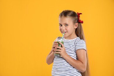Photo of Little girl drinking juice through straw on orange background, space for text