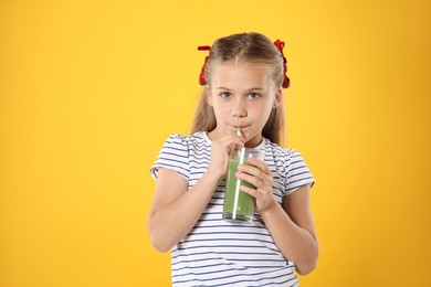 Photo of Little girl drinking juice through straw on orange background