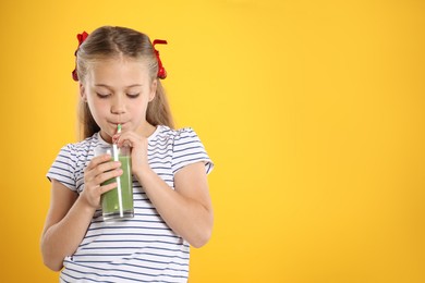 Photo of Little girl drinking juice through straw on orange background, space for text