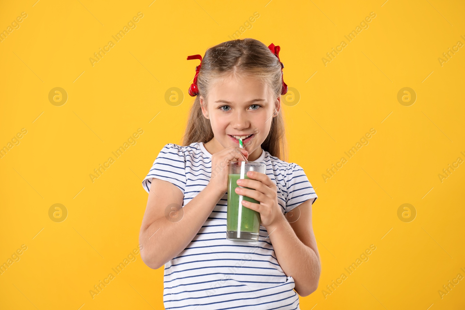 Photo of Little girl drinking juice through straw on orange background