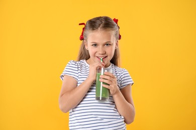 Photo of Little girl drinking juice through straw on orange background
