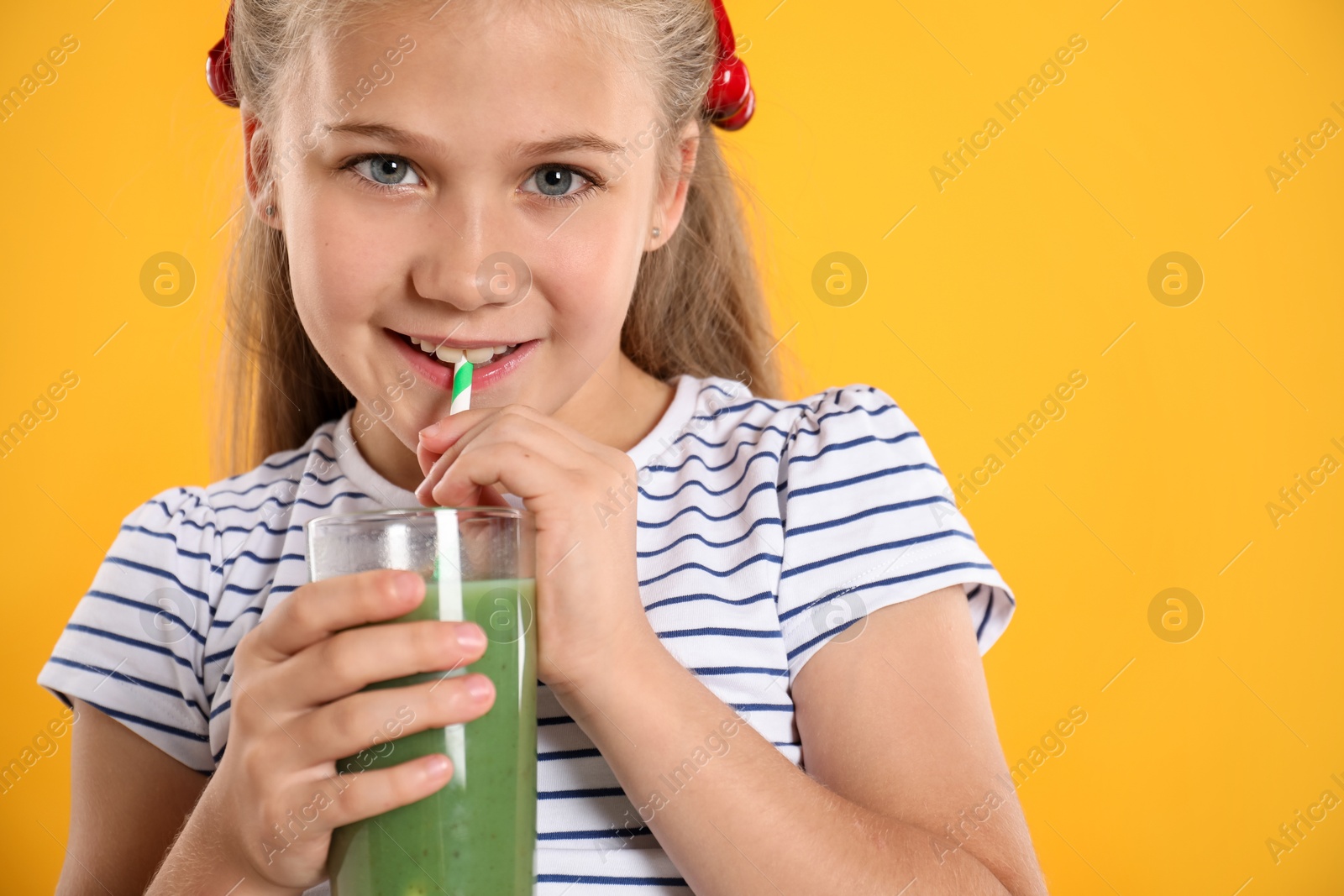 Photo of Little girl drinking juice through straw on orange background, space for text