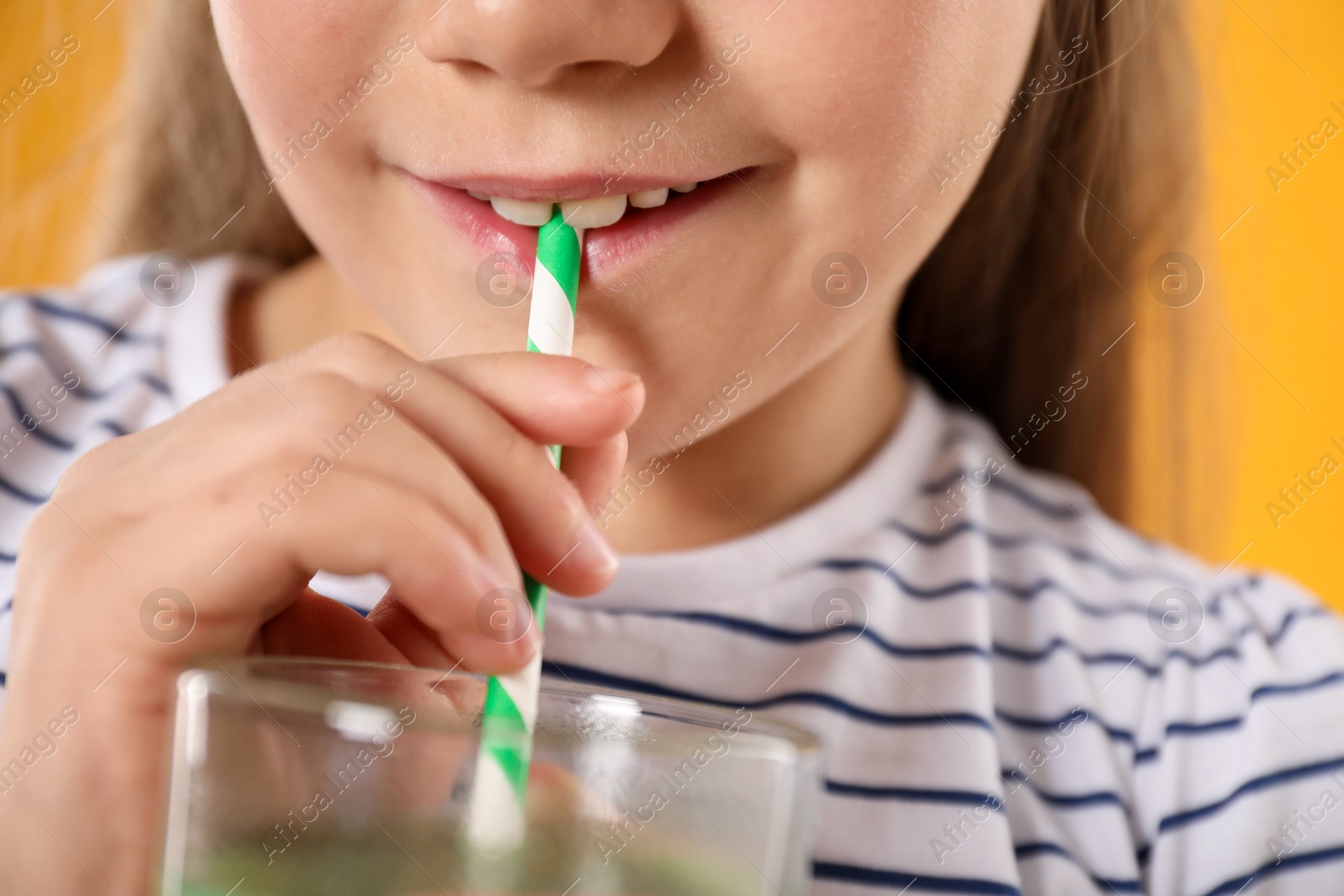 Photo of Little girl drinking juice through straw on orange background, closeup