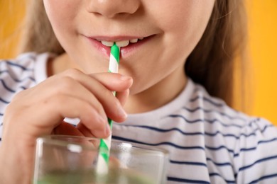 Photo of Little girl drinking juice through straw on orange background, closeup