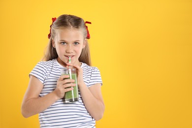 Photo of Little girl drinking juice through straw on orange background, space for text