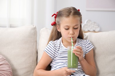 Photo of Little girl drinking juice through straw on sofa at home