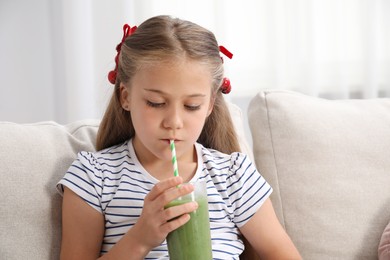 Photo of Little girl drinking juice through straw on sofa at home