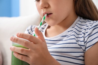 Photo of Little girl drinking juice through straw on sofa at home, closeup