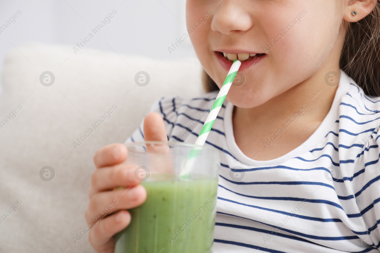 Little girl drinking juice through straw on sofa at home, closeup Photo of Little girl drinking juice through straw on sofa at home, closeup