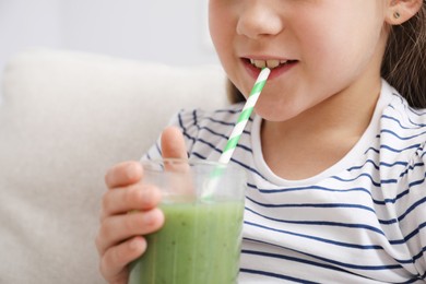 Photo of Little girl drinking juice through straw on sofa at home, closeup