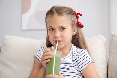 Photo of Little girl drinking juice through straw on sofa at home