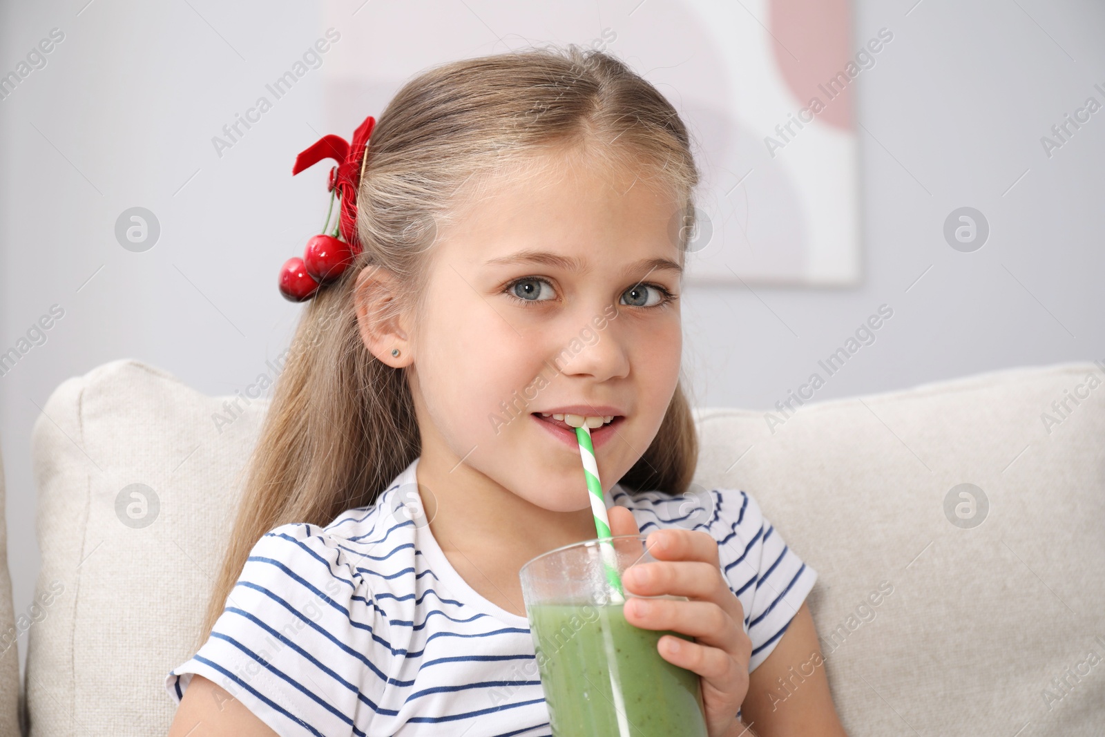 Photo of Little girl drinking juice through straw on sofa at home