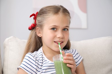 Photo of Little girl drinking juice through straw on sofa at home