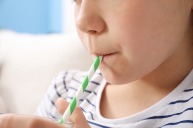 Photo of Little girl drinking refreshing drink through straw at home, closeup