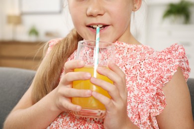 Photo of Little girl drinking juice through straw on sofa at home, closeup