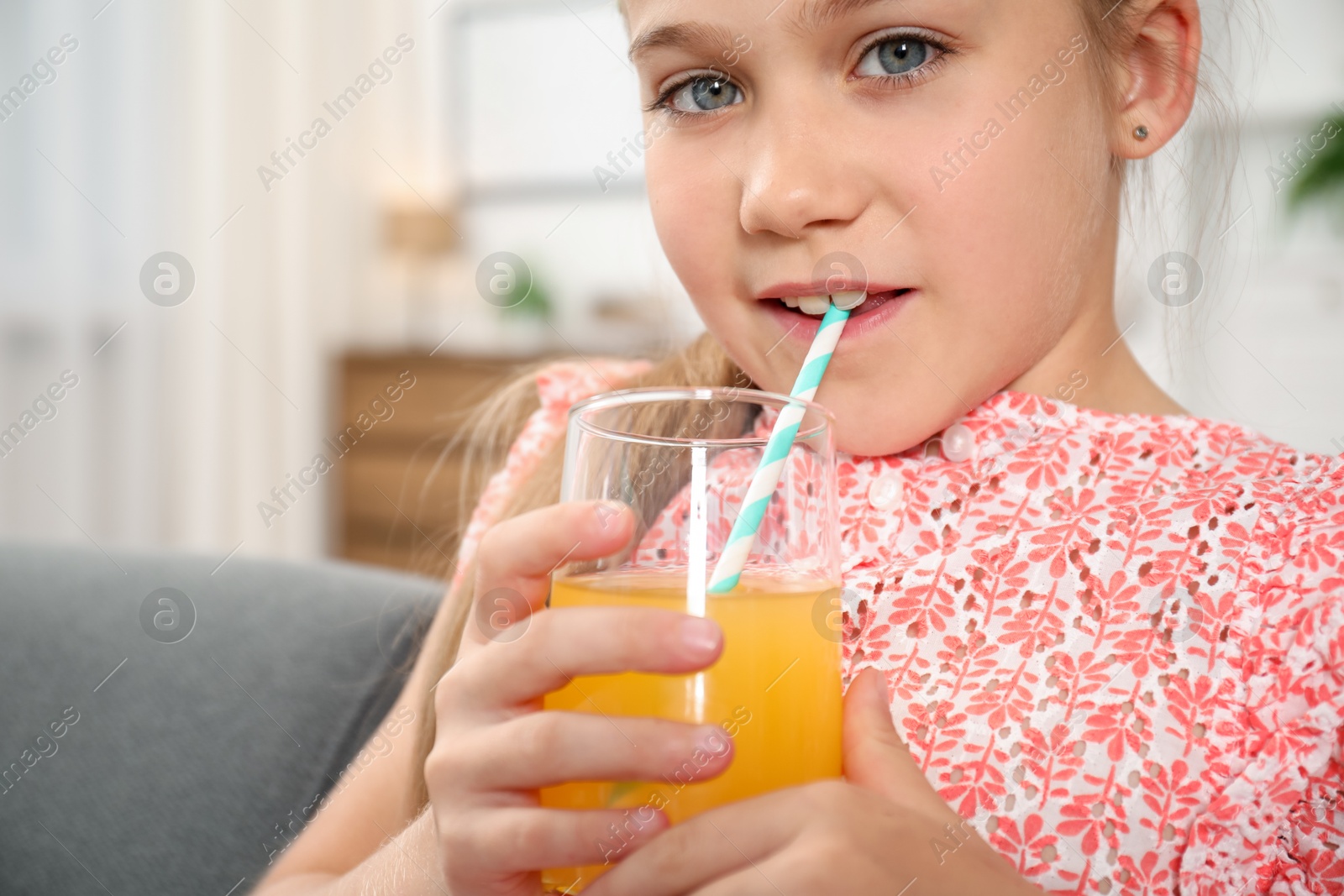 Photo of Little girl drinking juice through straw at home
