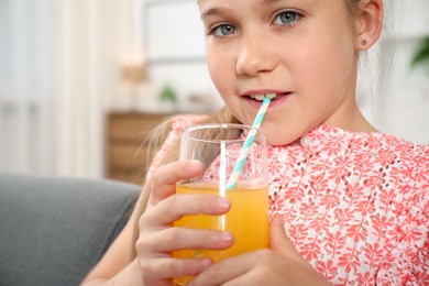 Photo of Little girl drinking juice through straw at home
