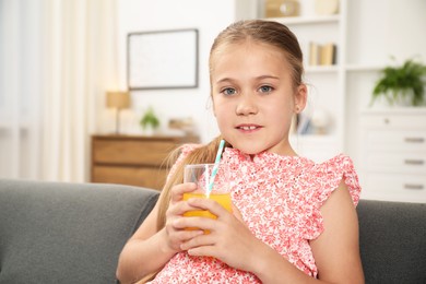 Photo of Little girl with juice and drinking straw on sofa at home