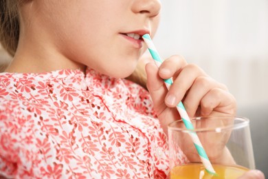Photo of Little girl drinking juice through straw at home, closeup