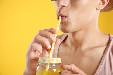 Photo of Man drinking juice through straw on orange background, closeup