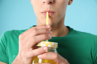 Photo of Man drinking juice through straw on light blue background, closeup