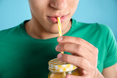 Photo of Man drinking juice through straw on light blue background, closeup