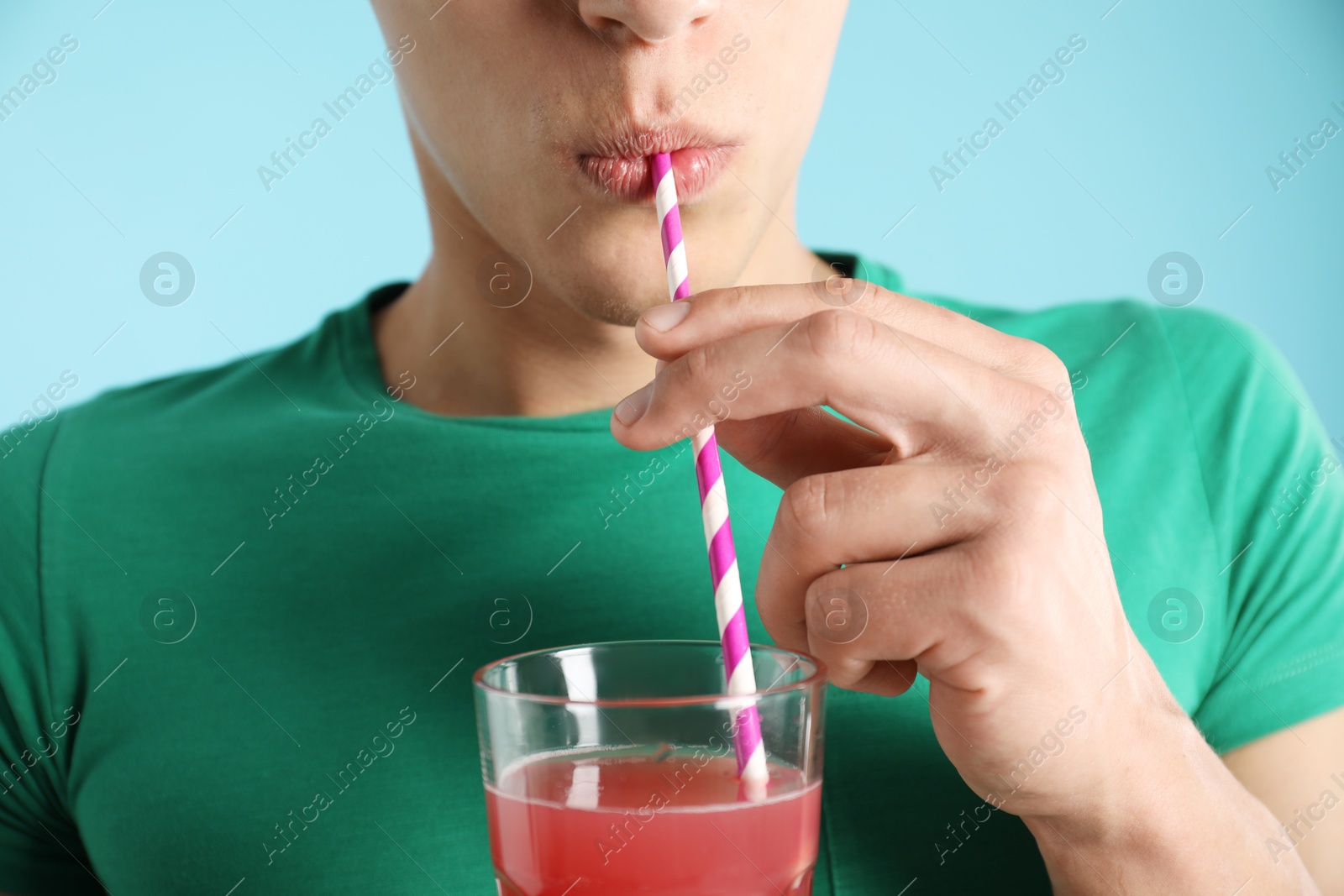 Photo of Man drinking juice through straw on light blue background, closeup