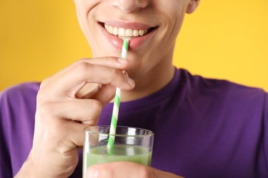 Photo of Man drinking juice through straw on orange background, closeup