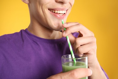 Photo of Man drinking juice through straw on orange background, closeup