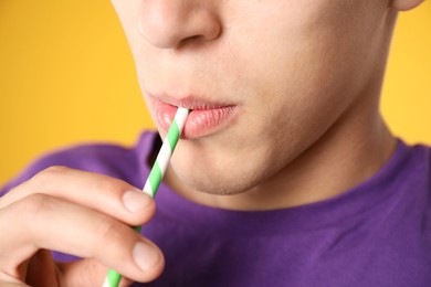 Photo of Man drinking refreshing drink through straw on orange background, closeup