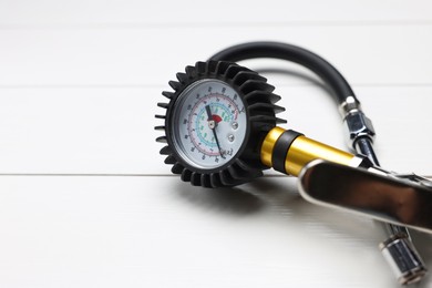 Photo of One tire inflation gun with gauge on light wooden table, closeup