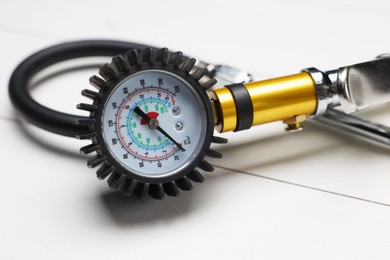 Photo of One tire inflation gun with gauge on light wooden table, closeup