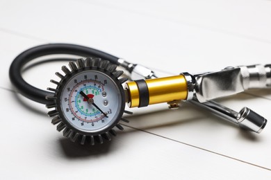 Photo of One tire inflation gun with gauge on light wooden table, closeup