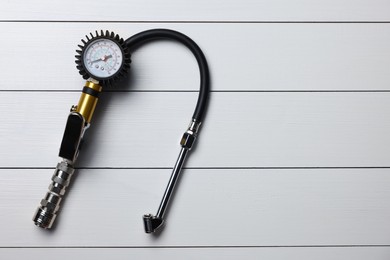 Photo of One tire inflation gun with gauge on light grey wooden table, top view. Space for text
