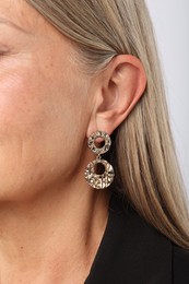 Photo of Woman wearing stylish earring on light background, closeup