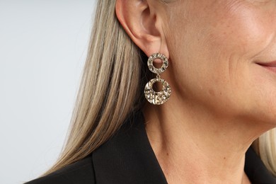 Photo of Woman wearing stylish earring on light background, closeup