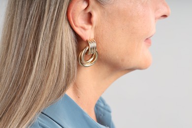 Photo of Woman wearing stylish earring on light background, closeup