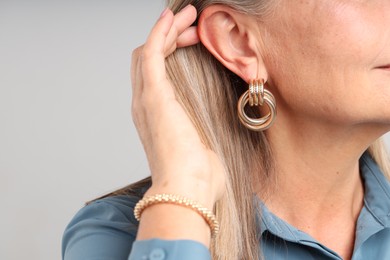 Photo of Woman wearing stylish earring and bracelet on light background, closeup