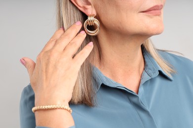 Photo of Woman wearing stylish earring and bracelet on light background, closeup