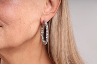 Photo of Woman wearing stylish earring on light background, closeup